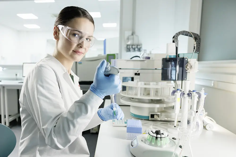 A female scientist is experimenting in a lab, wearing a lab coat and safety goggles.