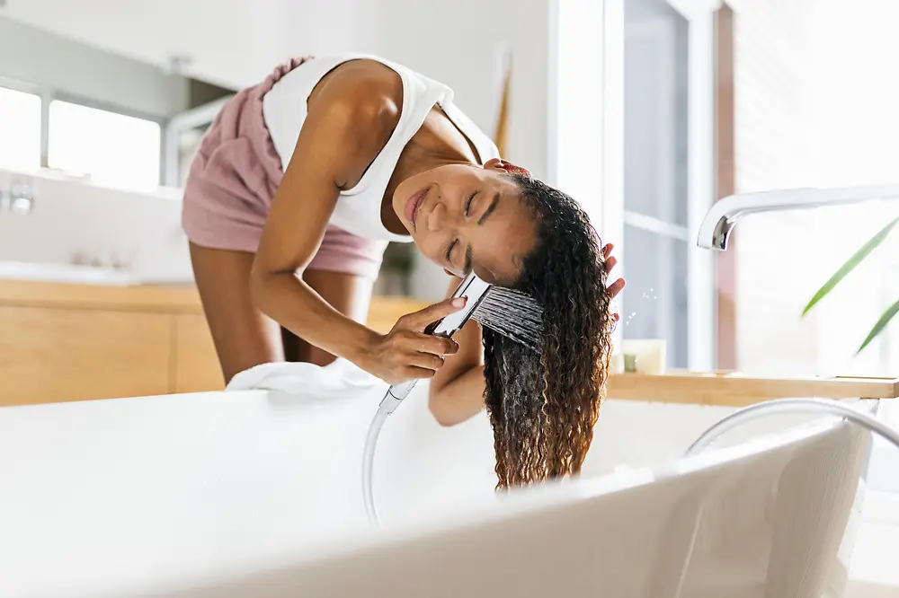 浴室のバスタブで茶色の長い髪を洗っている女性