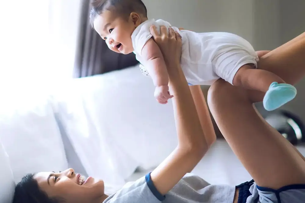 明るい家庭環境の中で、母親が笑顔の赤ちゃんを抱き上げて遊んでいる。