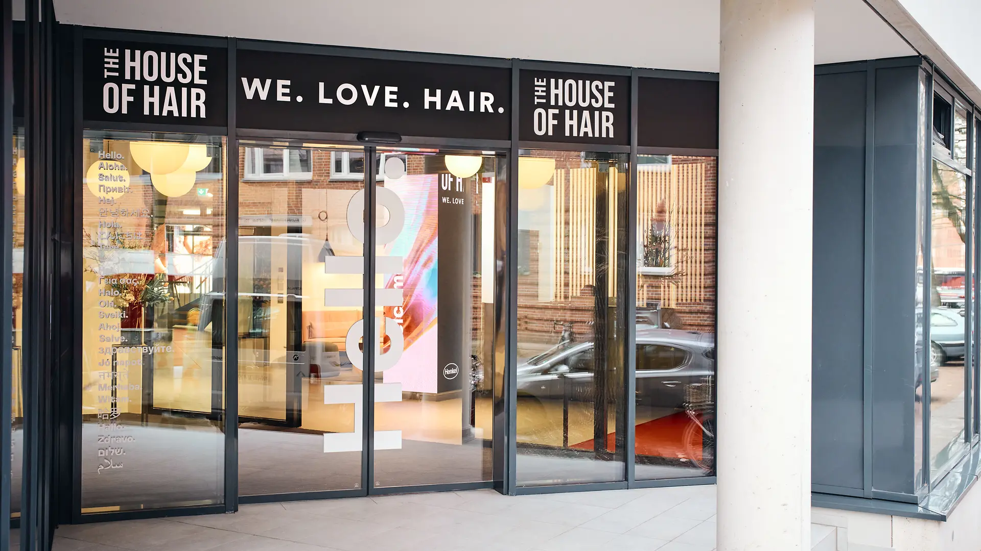 ガラス張りの玄関エリア。ドアの上にスローガン「We.Love.Hair」。その左右に「The House of Hair（ハウスオブヘア）」の文字。