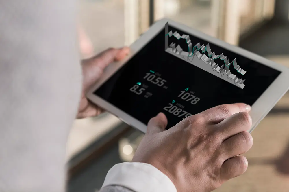 明るい室内で、デジタルチャートや数値データが表示されたタブレットを持つ人物を肩越しにのぞき込む写真。